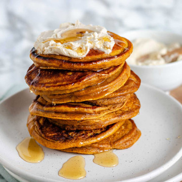A stack of pumpkin pancakes topped with whipped butter and maple syrup.