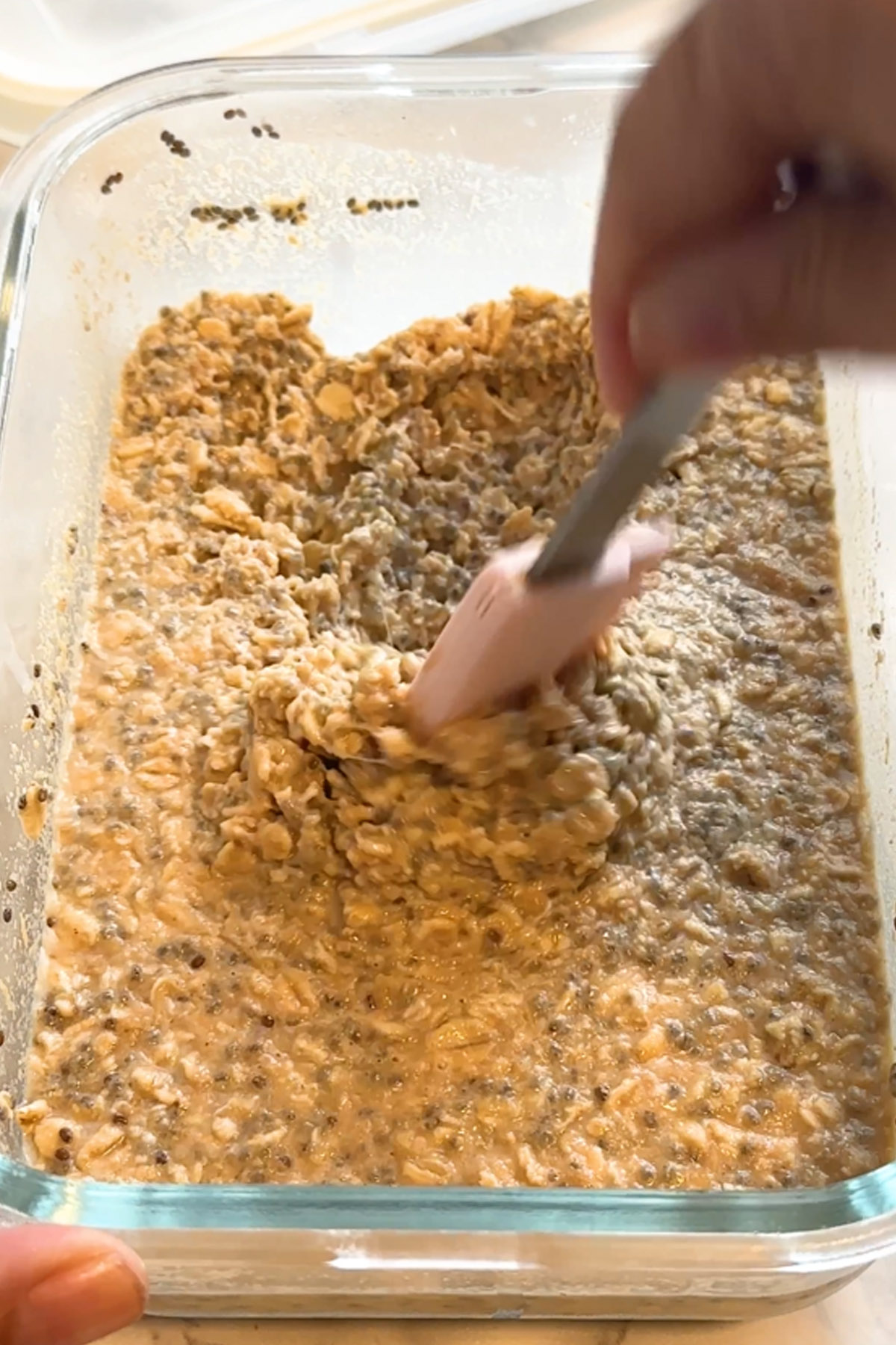 Thick, soaked oats are stirred with a small pink spatula.