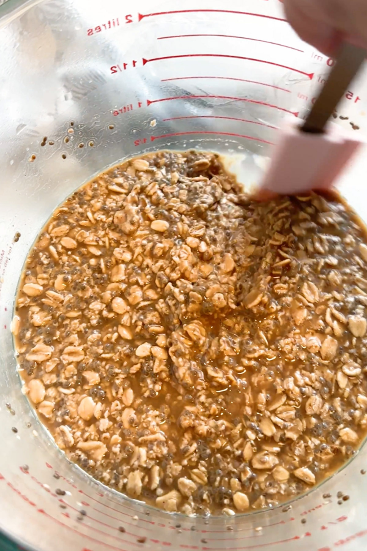 A thick oat mixture is stirred in a large glass measuring cup.