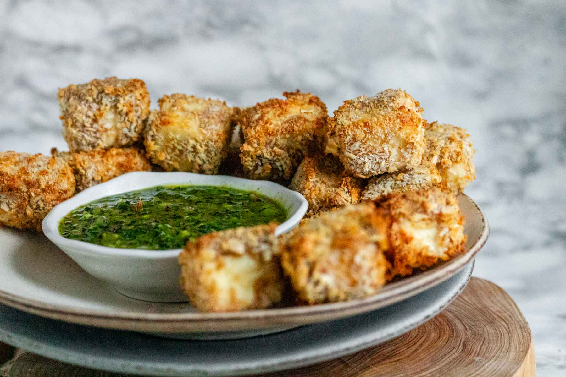 Breaded cubes of paneer on a plate with a green chimichurri sauce.
