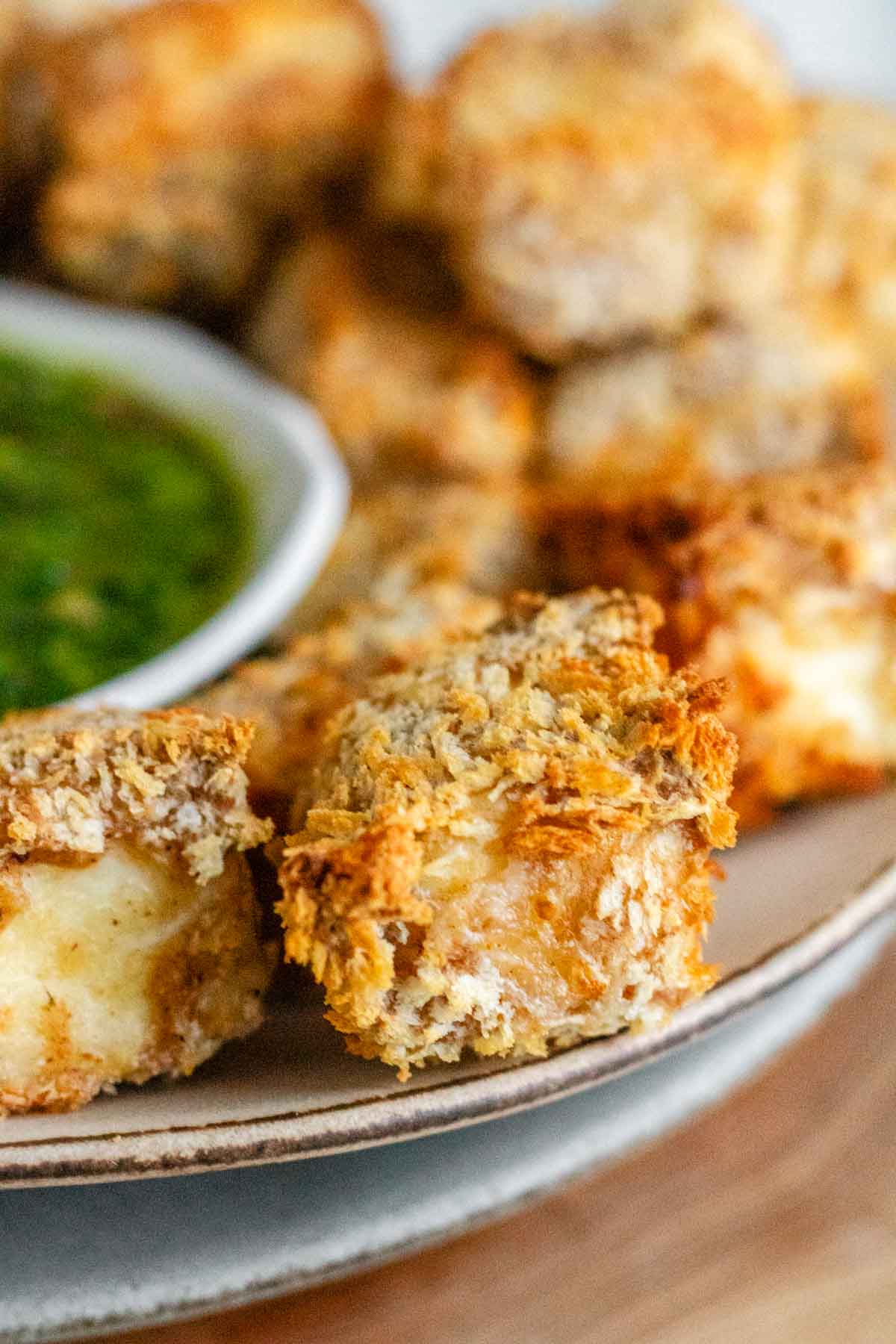 Breaded cubes of paneer on a plate with a green chimichurri sauce.