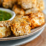 Breaded cubes of paneer on a plate with a green chimichurri sauce.
