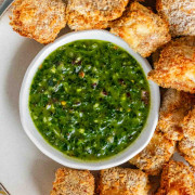 Breaded cubes of paneer on a plate with a green chimichurri sauce.