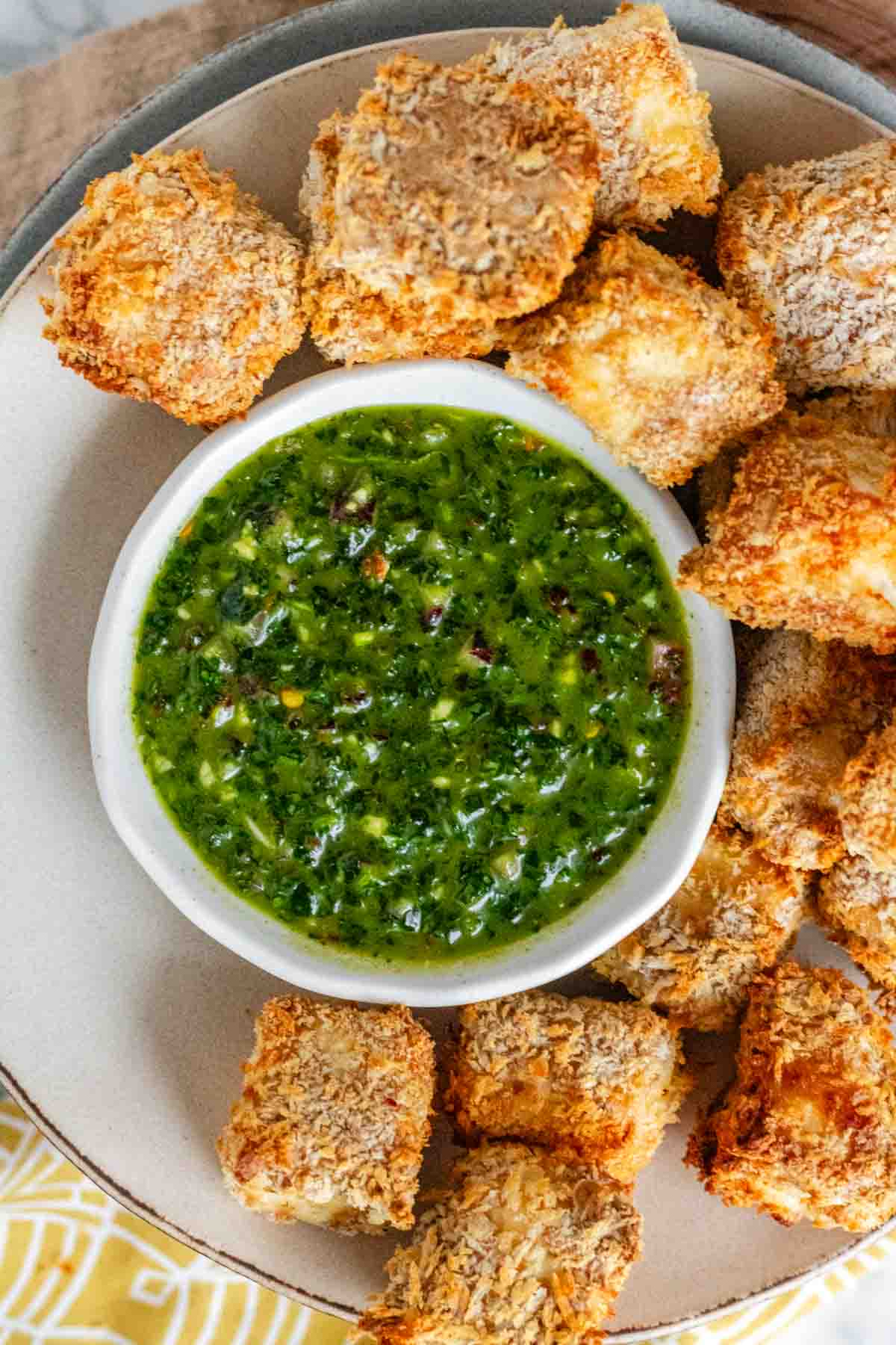 Breaded cubes of paneer on a plate with a green chimichurri sauce.