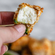 A cube of breaded paneer with a bite it in is held up by hand.