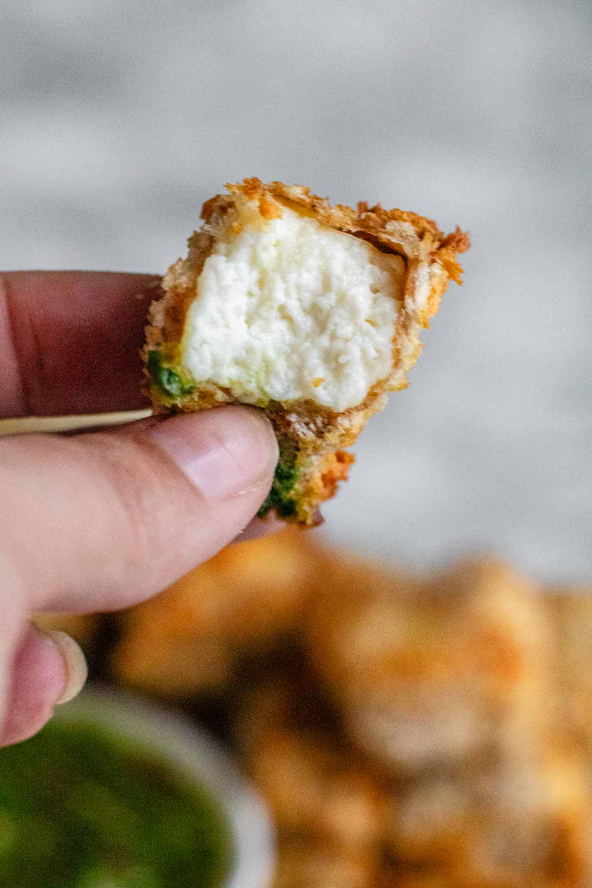 A cube of breaded paneer with a bite it in is held up by hand.
