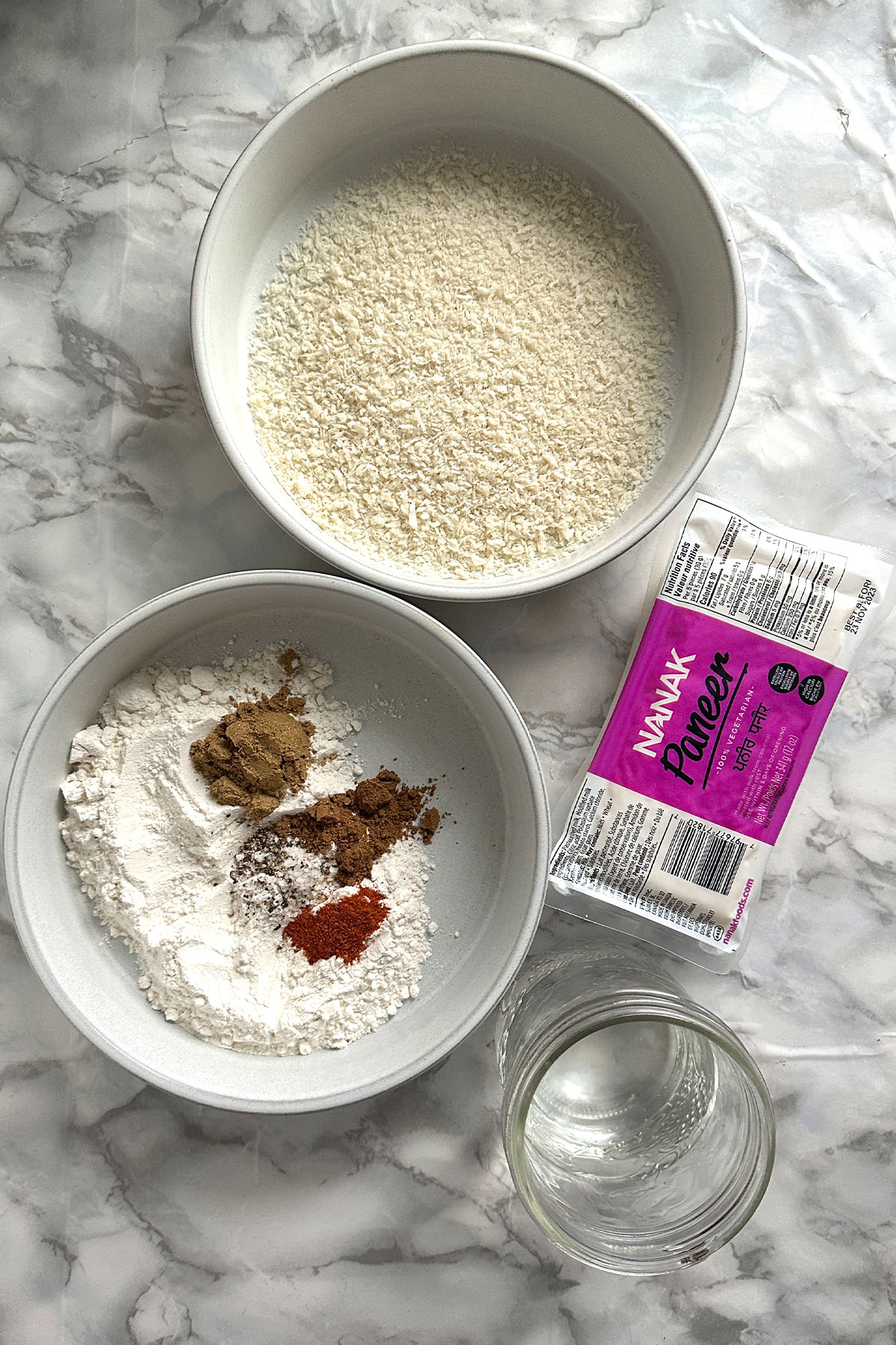 Ingredients for breading paneer sit on a white marble counter.