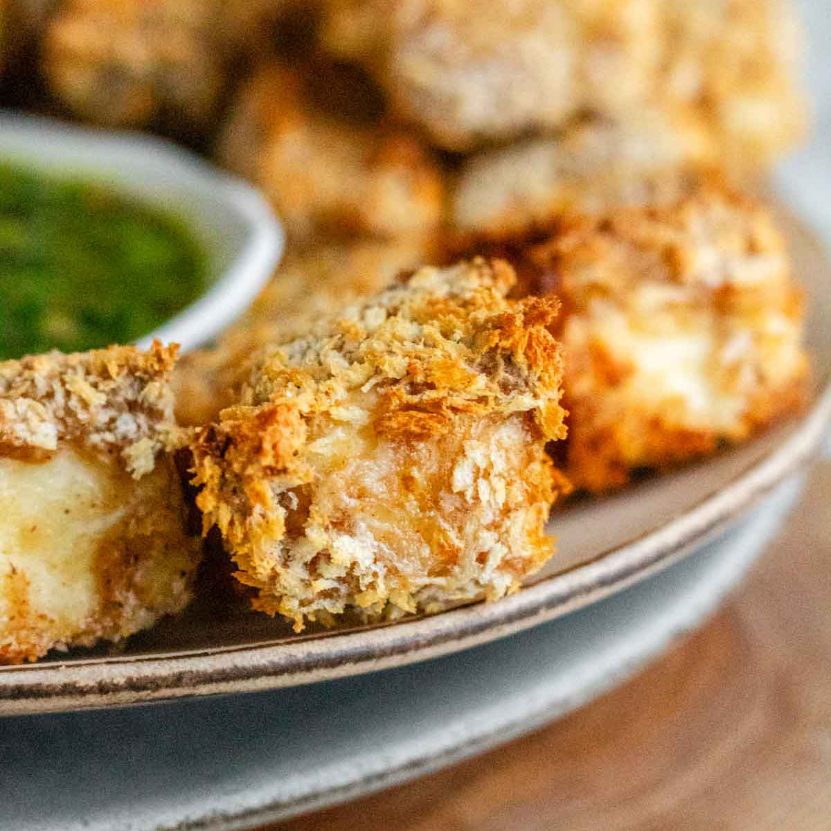 Breaded cubes of paneer on a plate with a green chimichurri sauce.