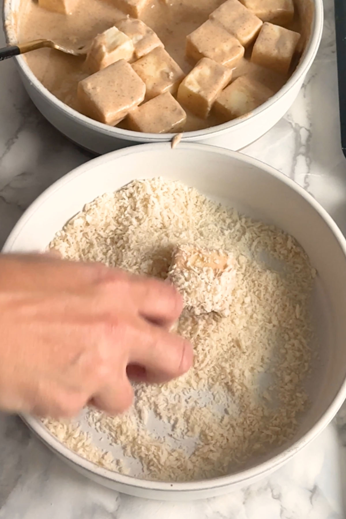 A cube of paneer is coated in bread crumbs.