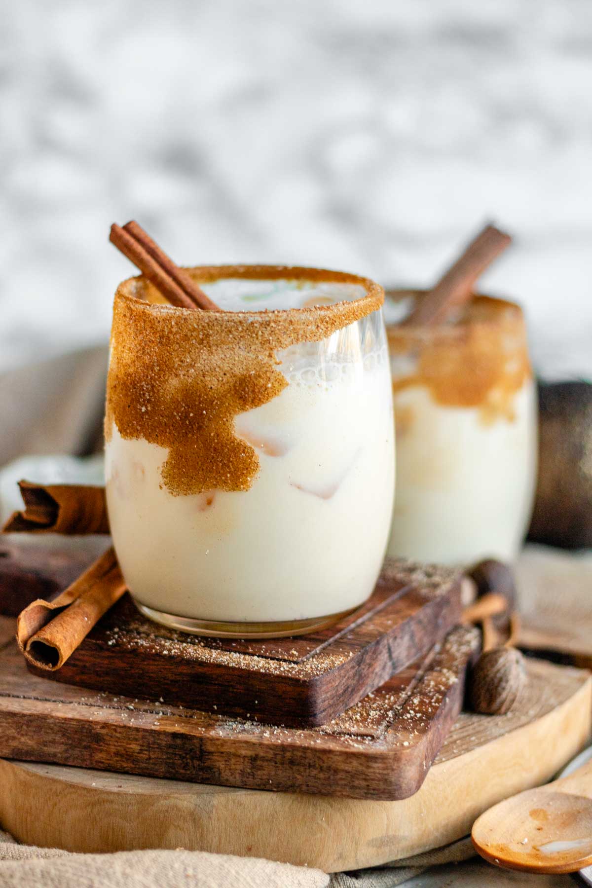 Eggnog in a glass rimmed with sugar and cinnamon with a cinnamon stick as garnish.