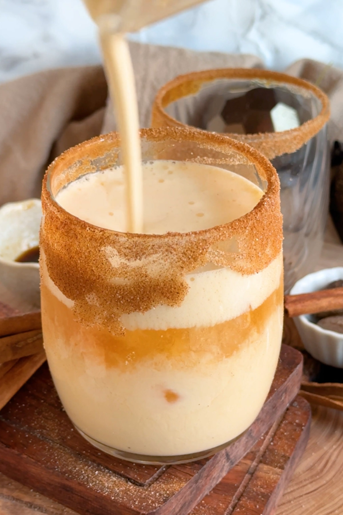 Frothed eggnog is poured on top of a bourbon eggnog cocktail in a glass rimmed with cinnamon sugar.