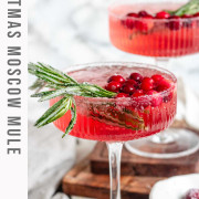 A pink cocktail in glasses garnished with sugared cranberries and rosemary with text for Pinterest.