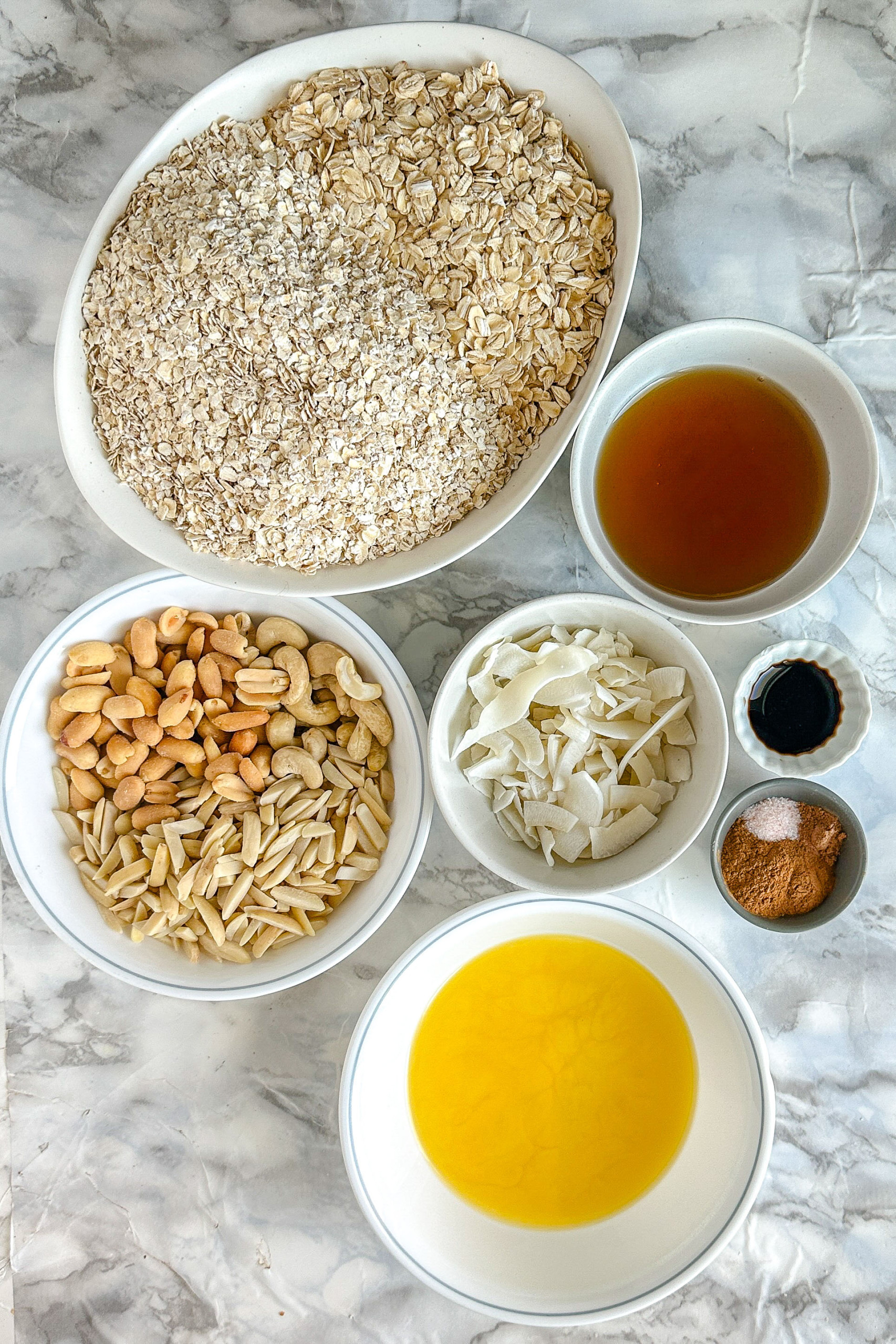 Ingredients for granola in bowls on a white marble counter.