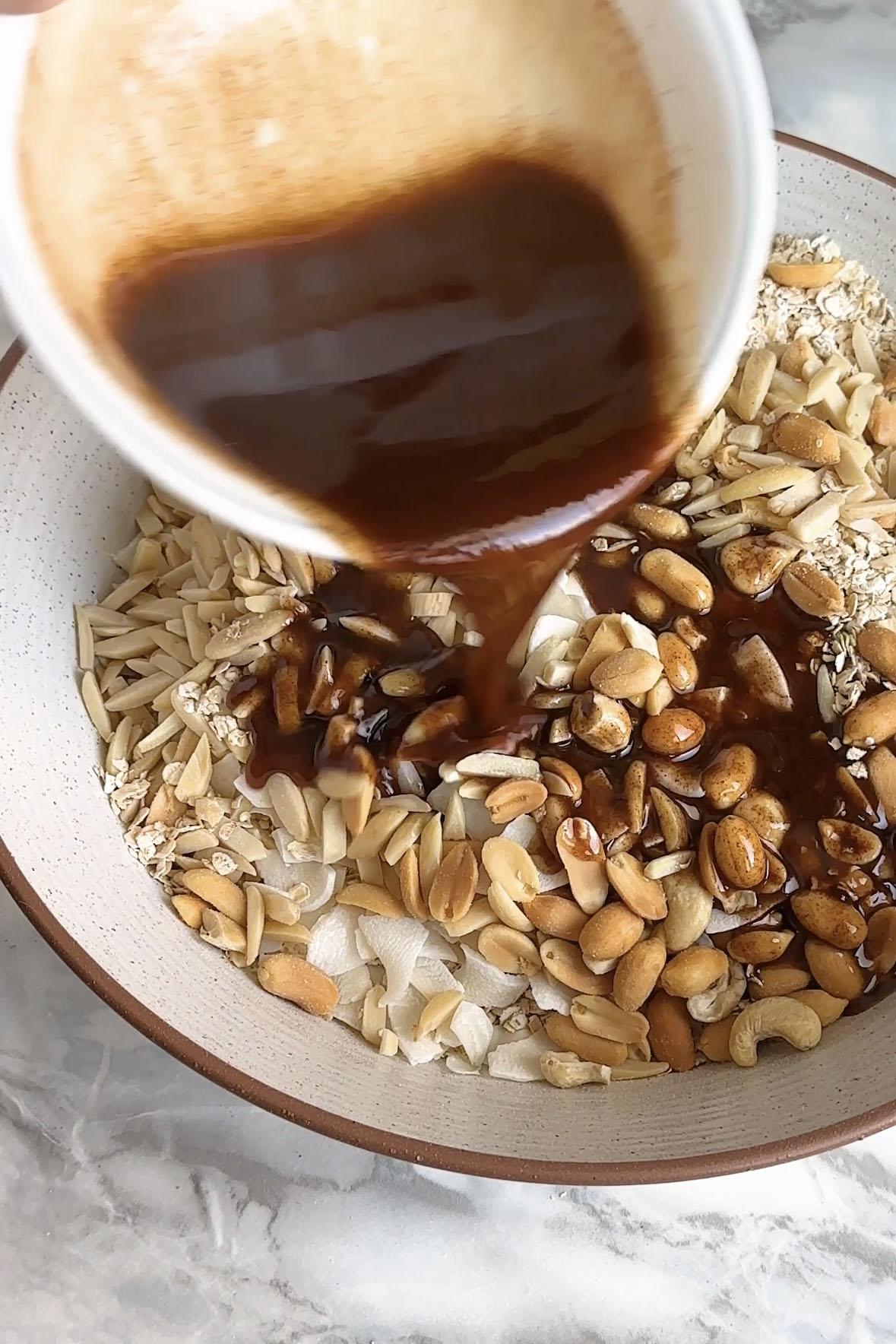 Cinnamon butter is poured onto oats and nuts to make granola.