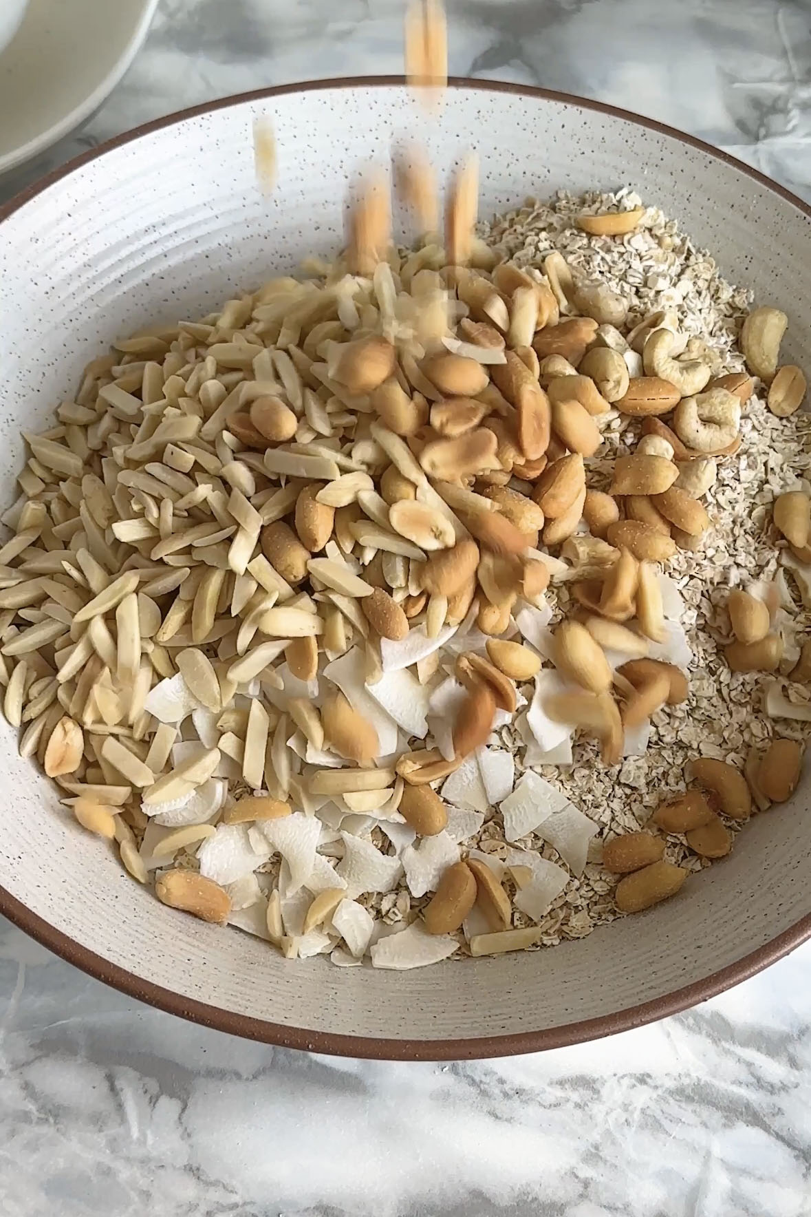 Nuts are poured on top of oats and coconut in a large bowl.