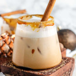 A creamy drink in a rimmed glass with a cinnamon stick in it.