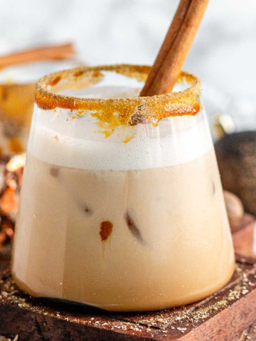 A creamy drink in a rimmed glass with a cinnamon stick in it.