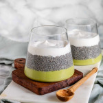 A layered dessert in a cup with a green avocado layer on the bottom, chia layer in the middle and white cream layer on top.