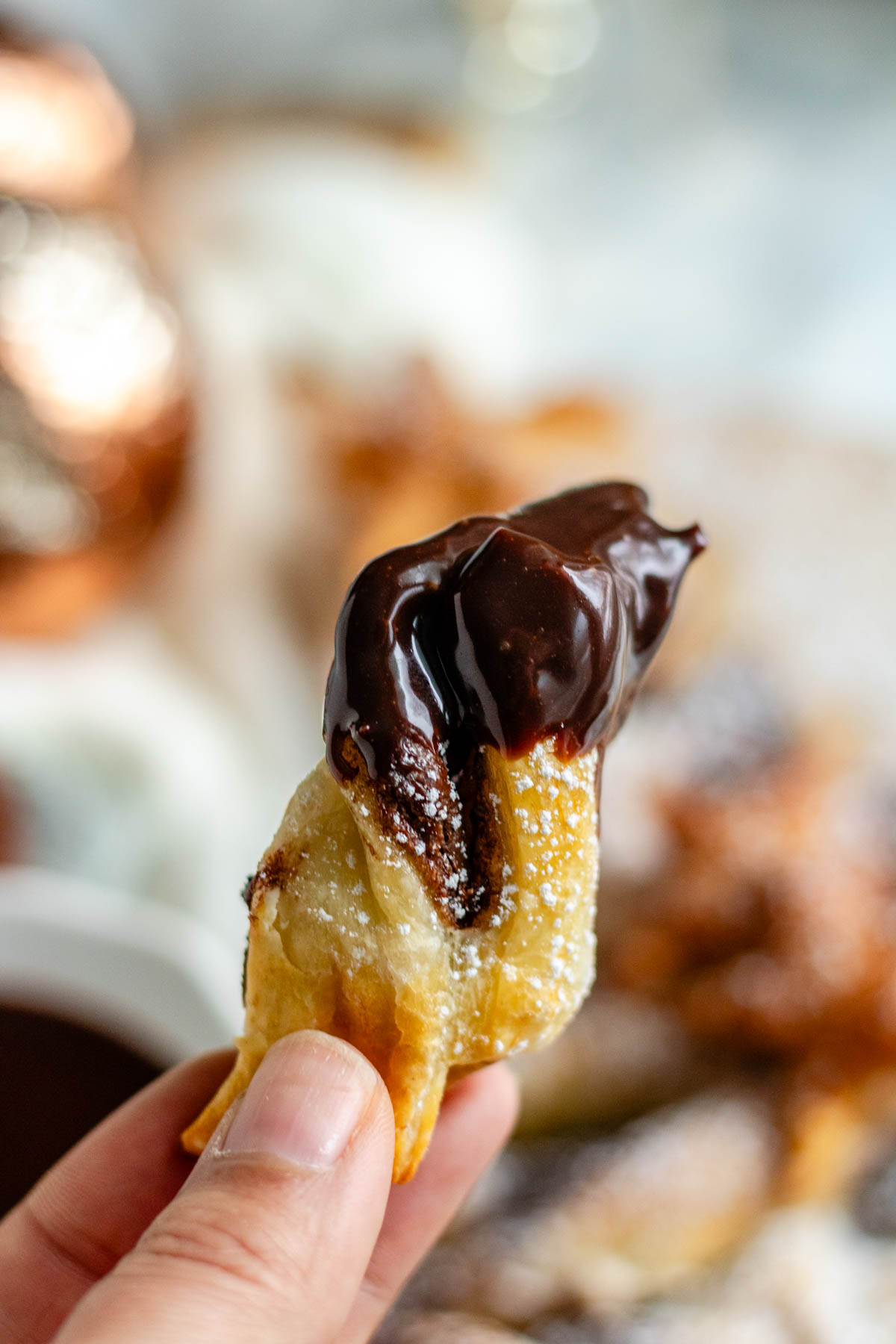 A piece of puff pastry with chocolate dip on it is held up by hand.