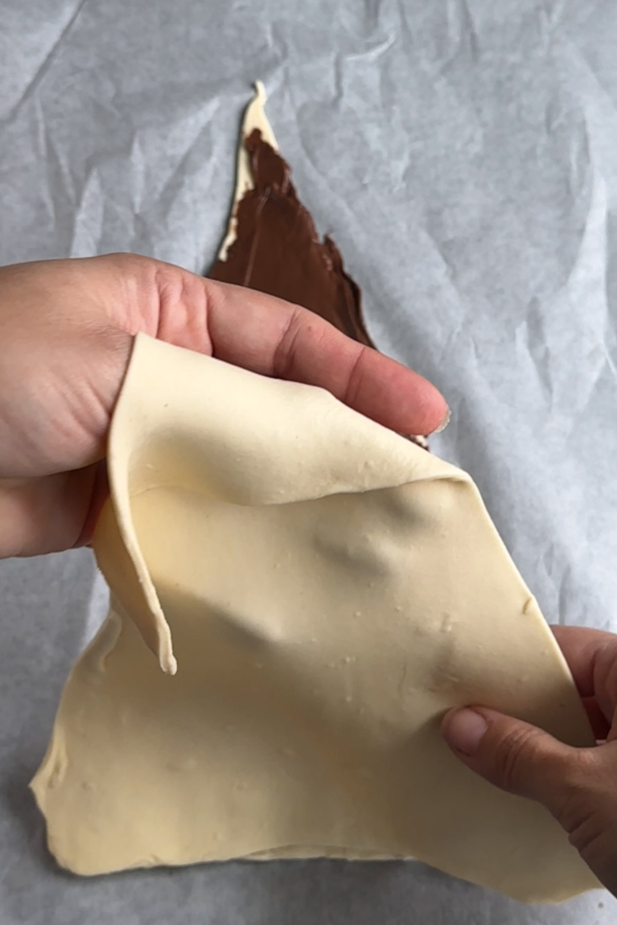 A sheet of pastry is placed on top of a Nutella covered sheet of pastry.