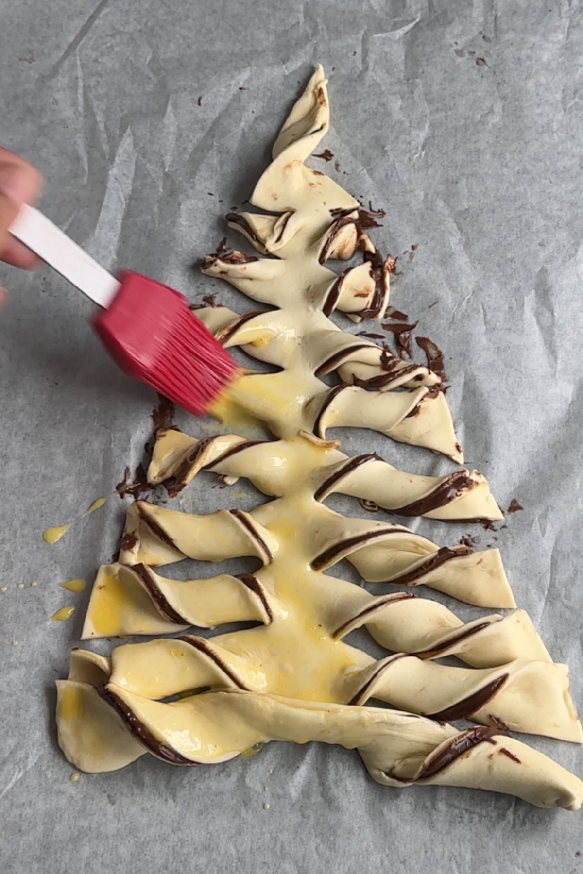 Egg is brushed onto a Nutella puff pastry tree before baking.