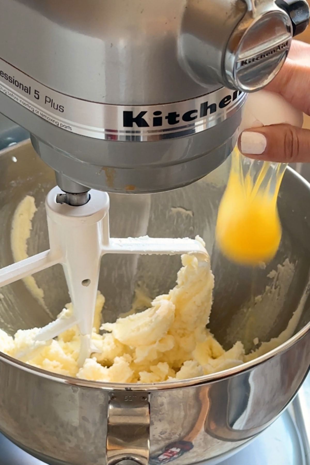 An egg is added to a stand mixer with whipped butter and sugar in it.