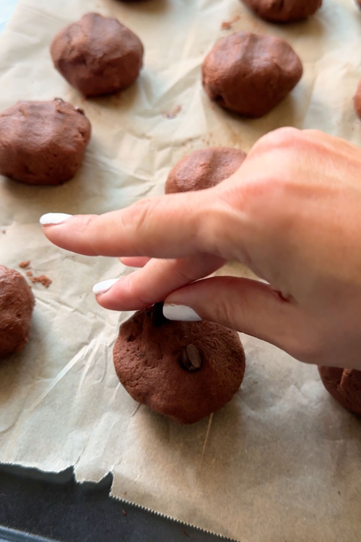 Chocolate chips are pressed into the top of a chocolate cookie dough ball.