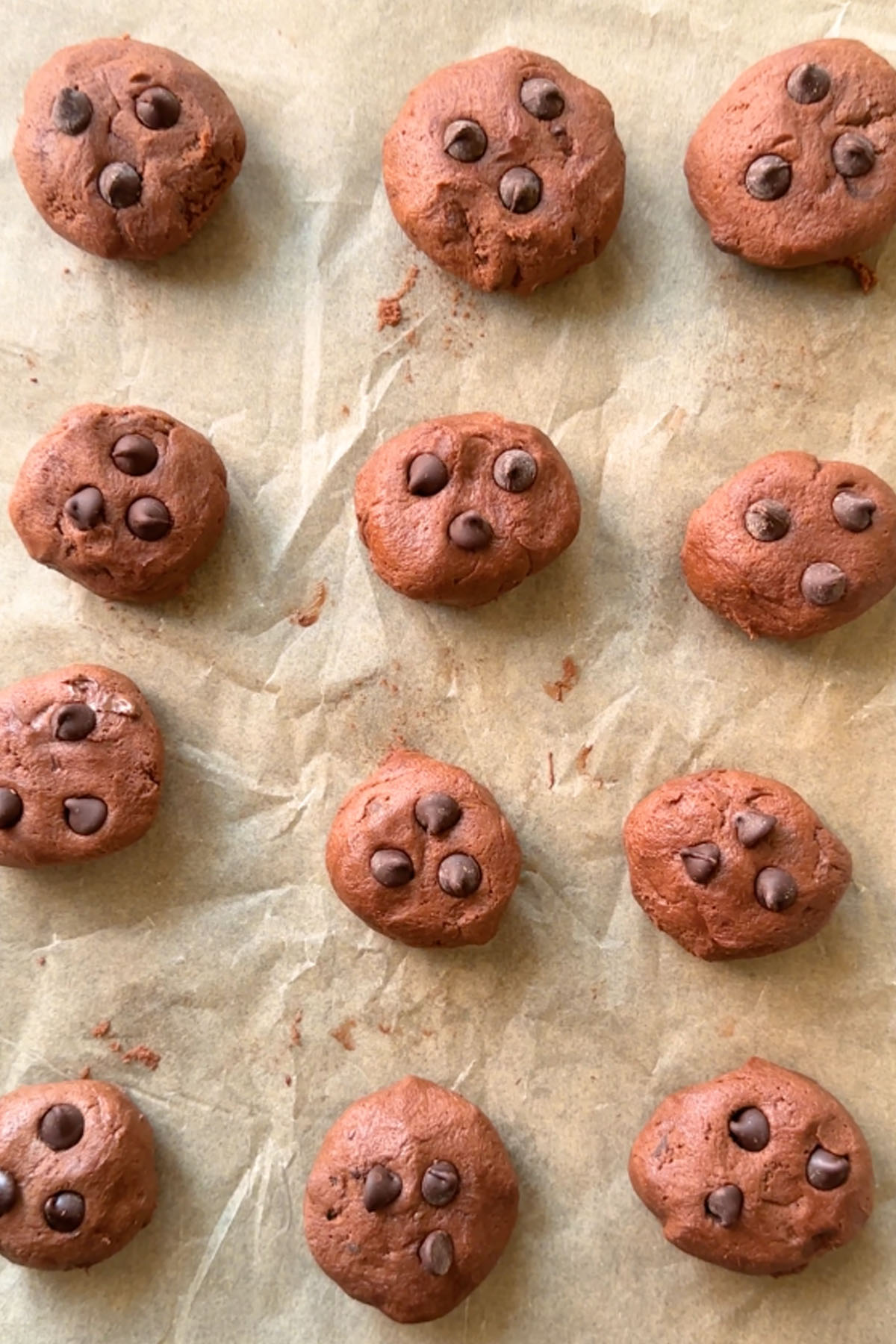 12 chocolate cookie dough balls are set evenly on a parchment lined baking sheet.