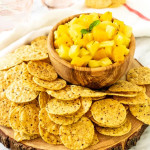 Mango and pineapple salsa in a bowl with chips on a platter surrounding it with a text title for Pinterest.