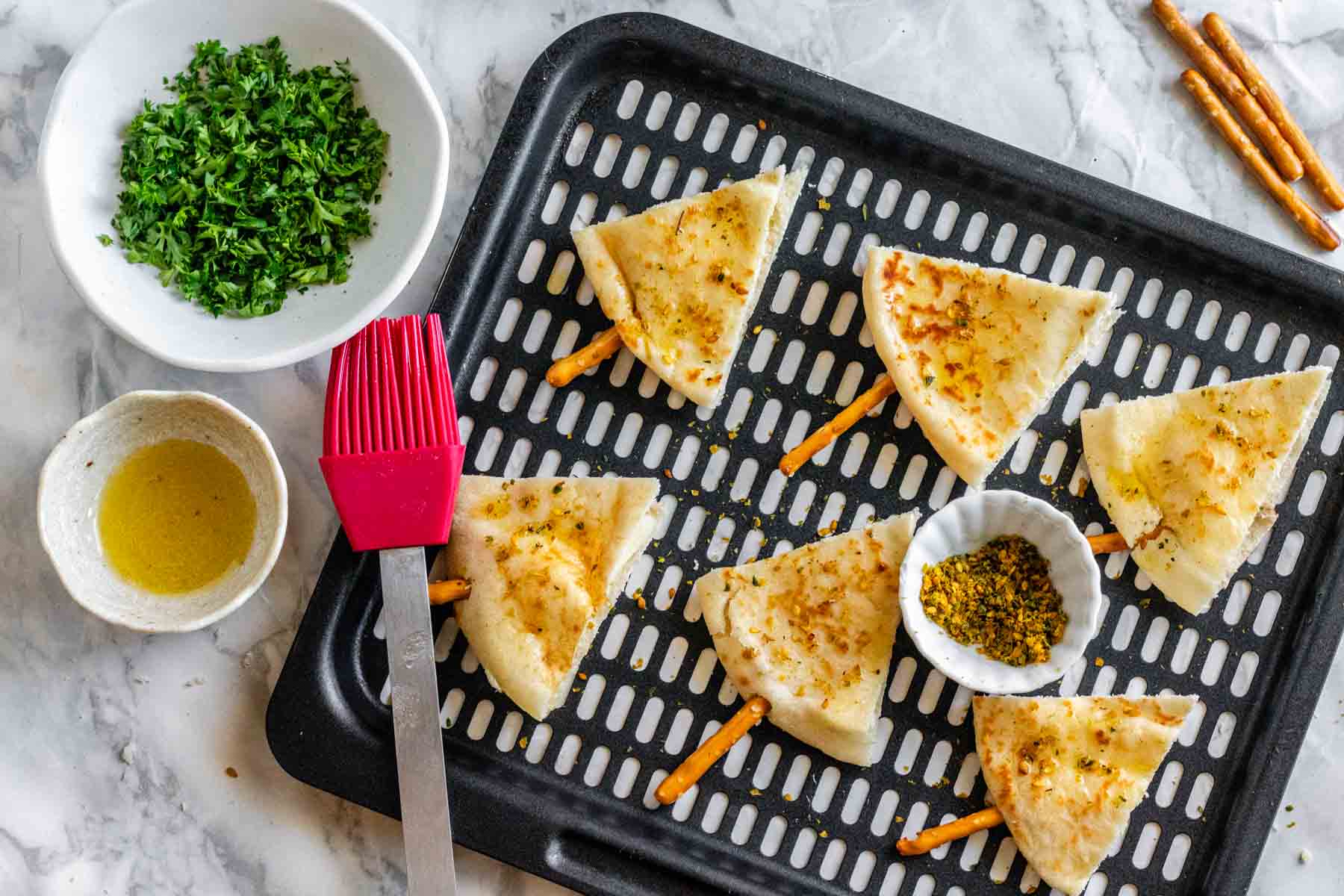 Pita triangles lay on an air fryer baking sheet with oil and za'atar seasoning on top.
