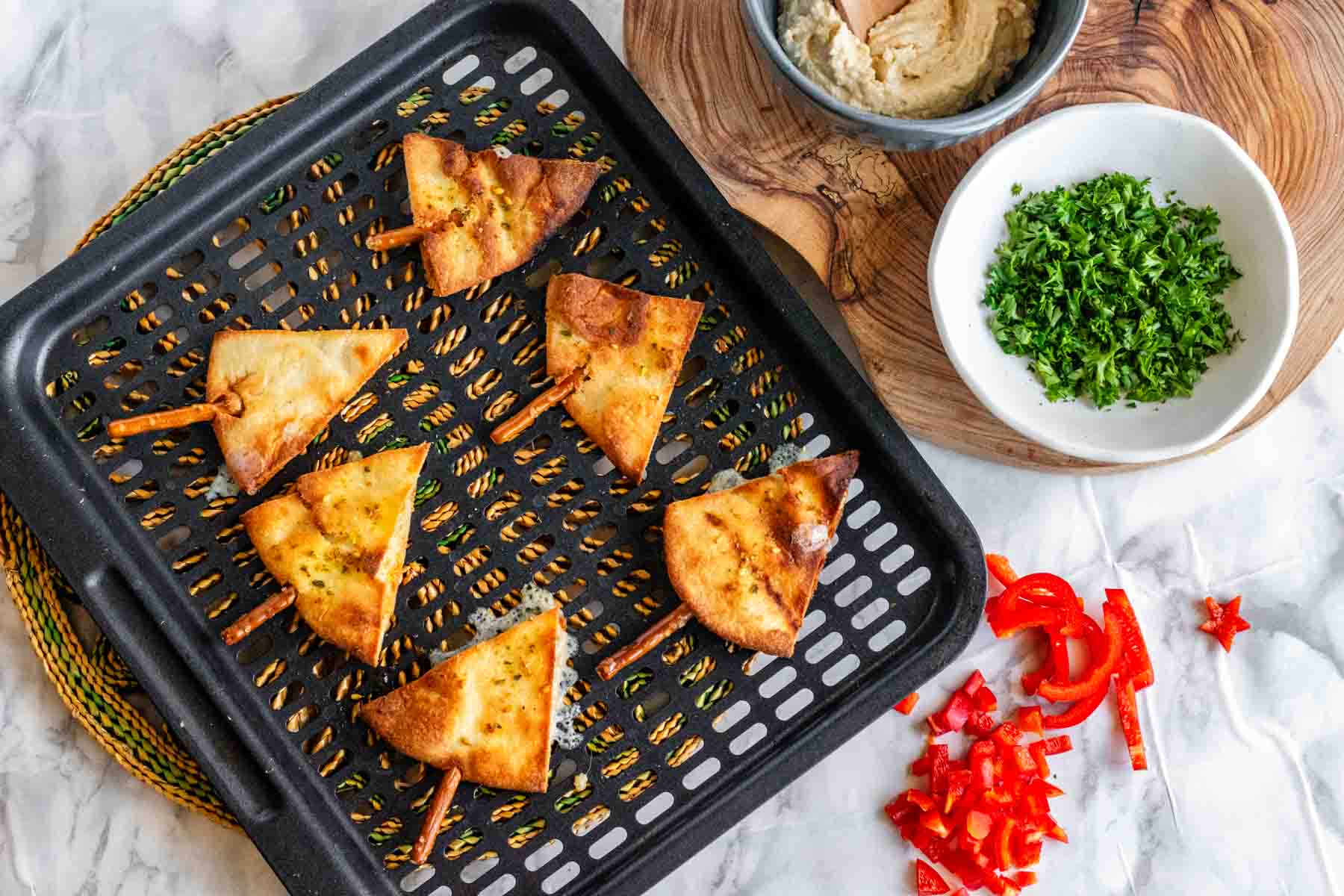 Baked pita triangles lay on an air fryer baking sheet with oil and za'atar seasoning on top.