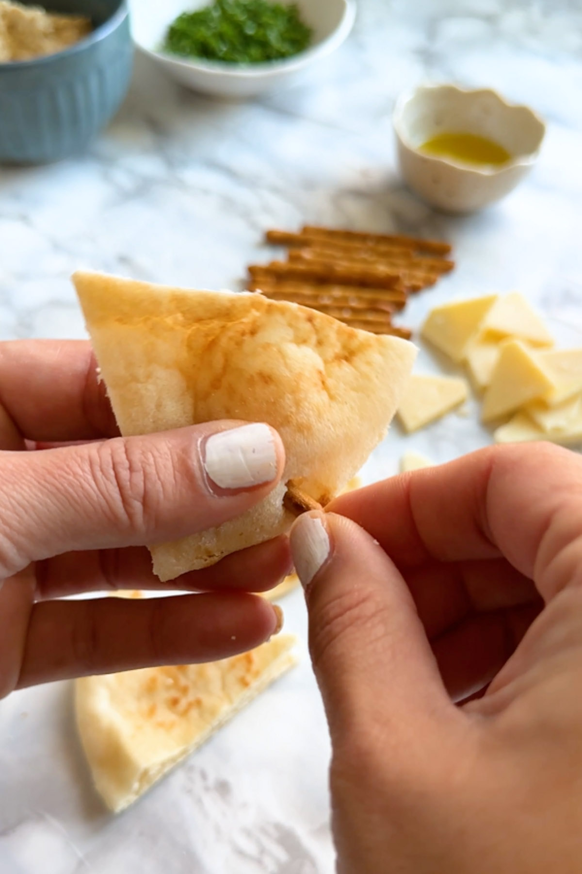 Poking a pretzel into the bottom of a pita wedge by hand.