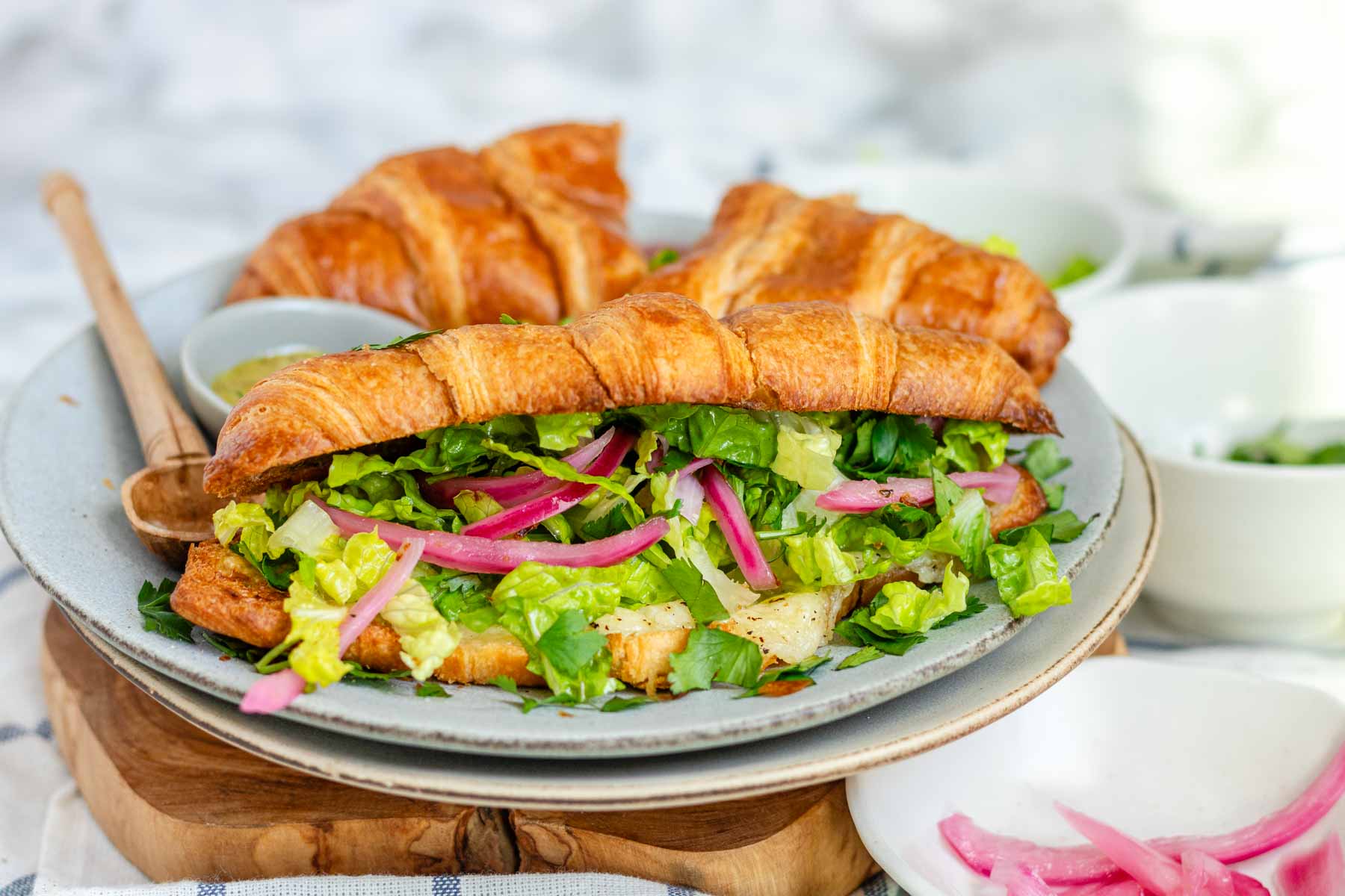 A croissant sandwich with cheese, lettuce, and pickled red onions.