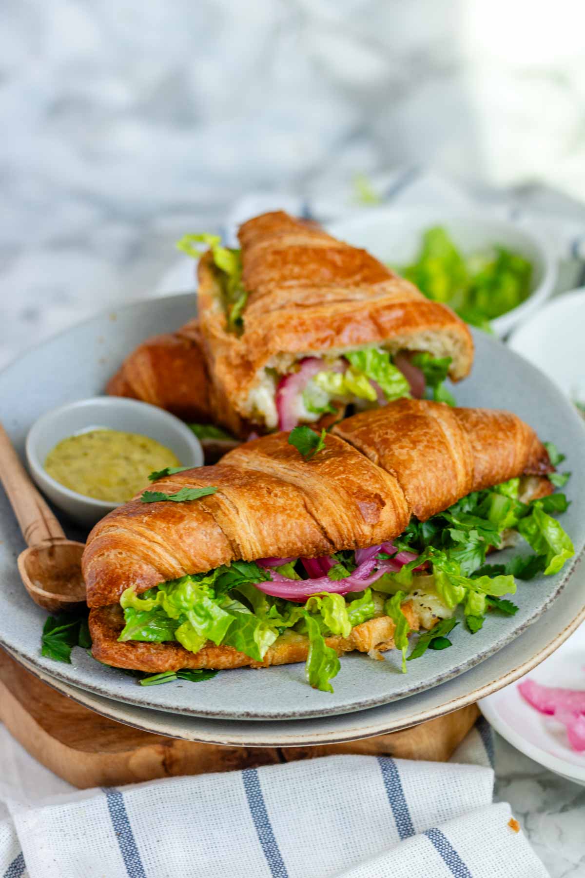 A croissant sandwich with cheese, lettuce, and pickled red onions.