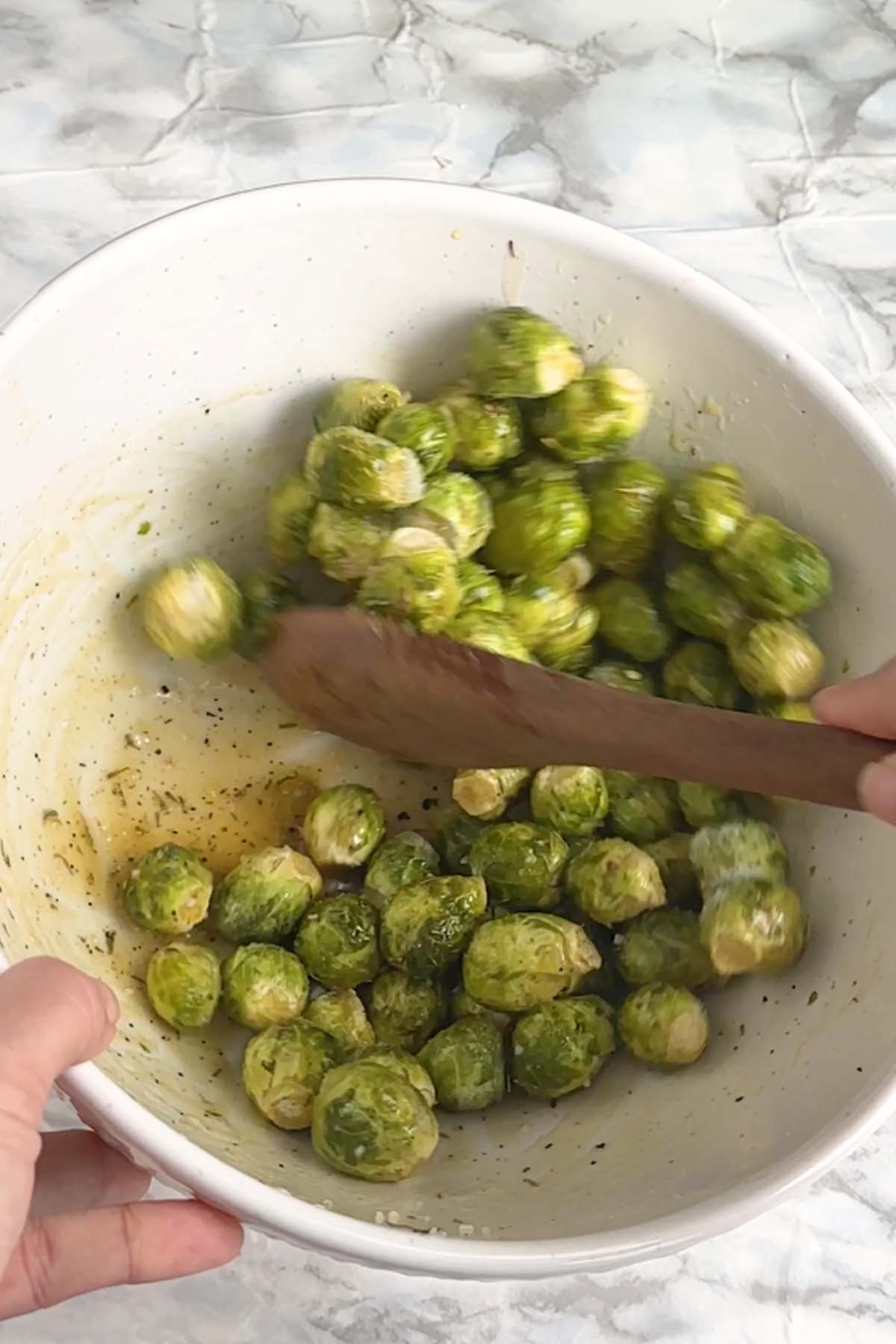 Brussels sprouts are mixed with a sauce in a large bowl.