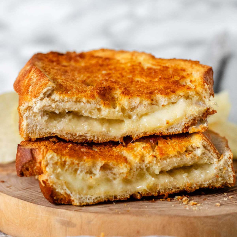A cross-section of a grilled cheese sandwich on a wooden platter with potato chips.
