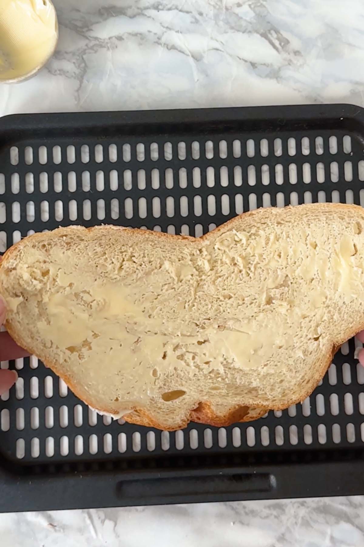 A piece of buttered bread on an air fryer tray.