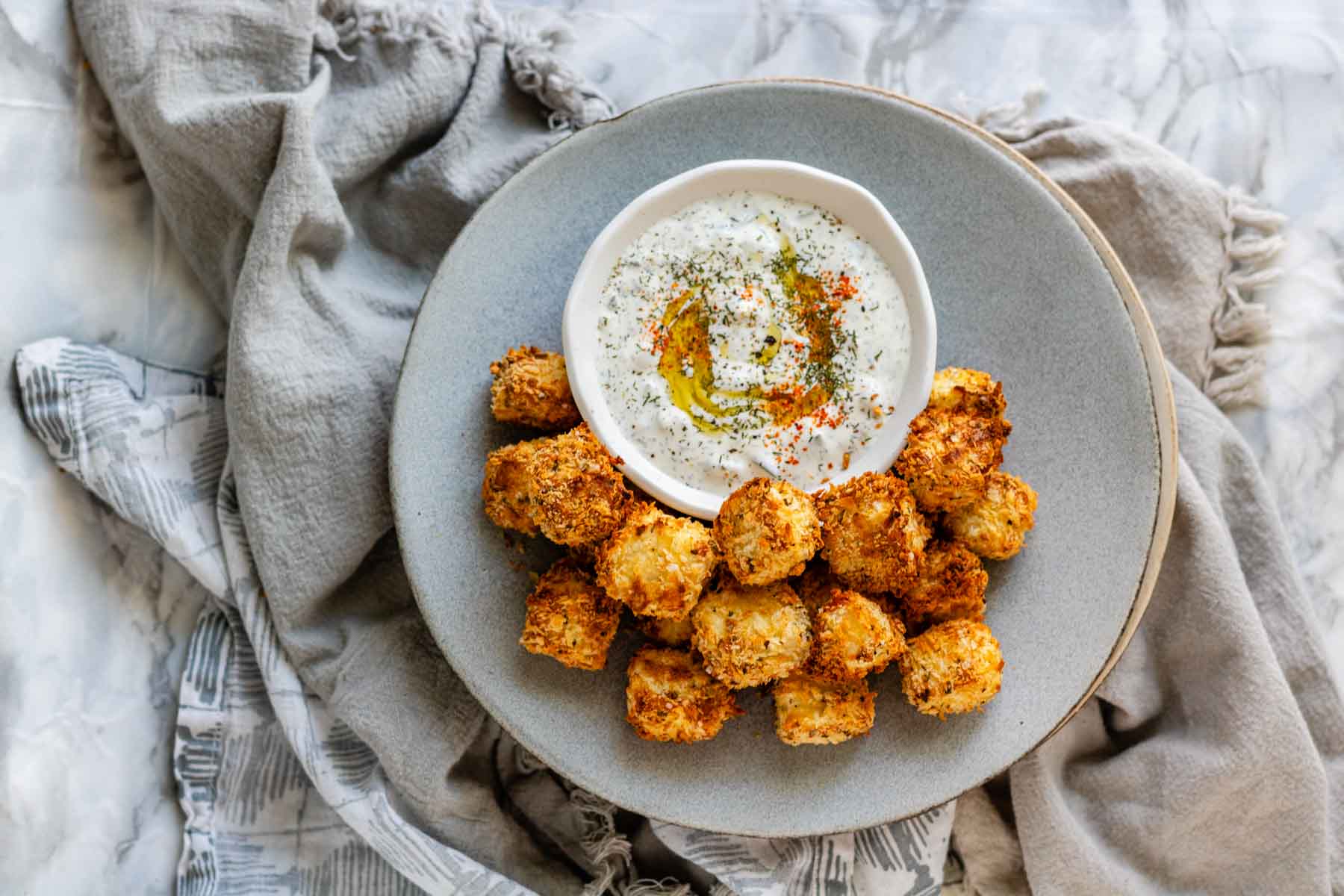 Breaded halloumi cubes on a plate with a bowl of dip.