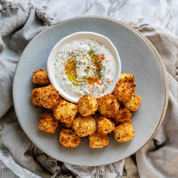 Breaded halloumi cubes on a plate with a bowl of dip.