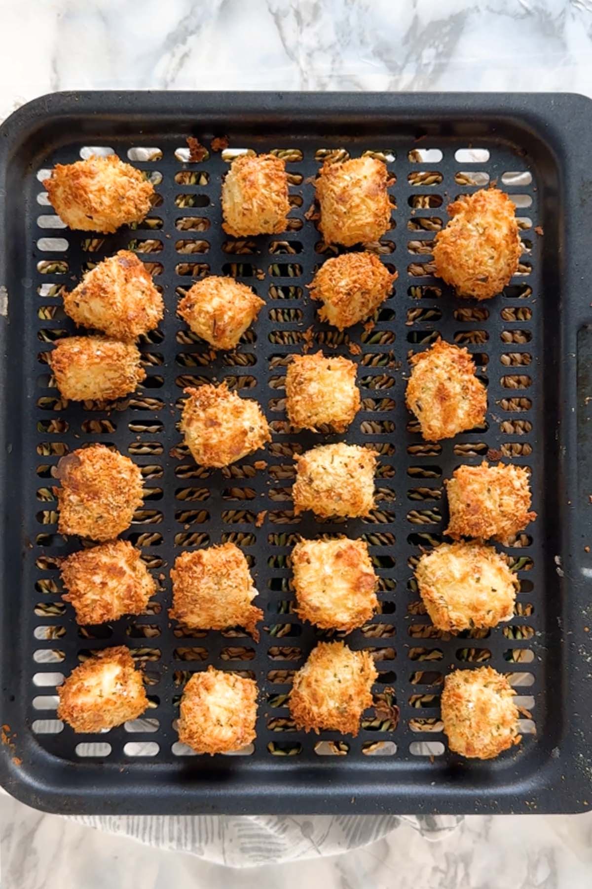 Cooked breaded halloumi bites on an air fryer tray.