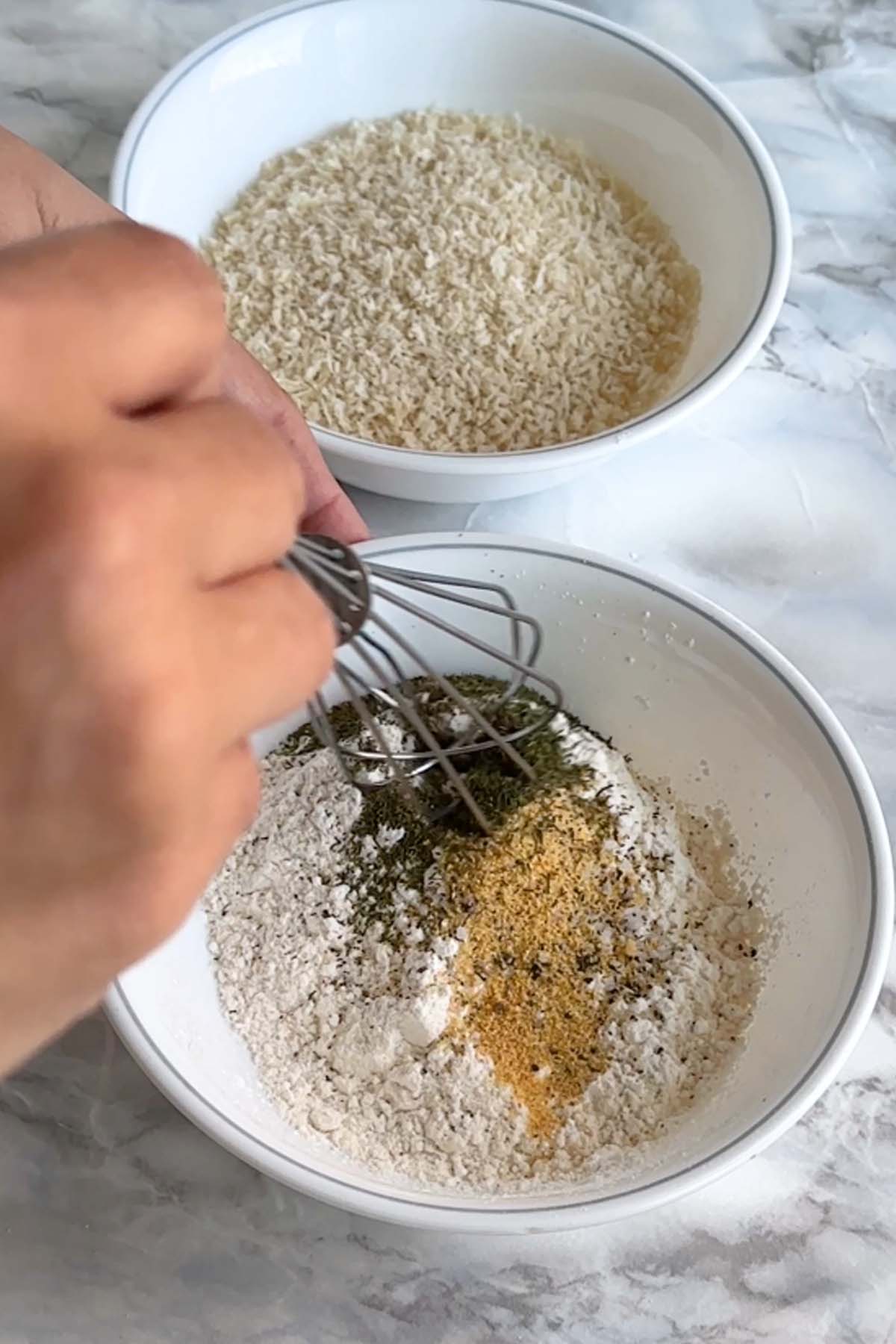 A bowl with breadcrumbs and a bowl of flour and spices being whisked.