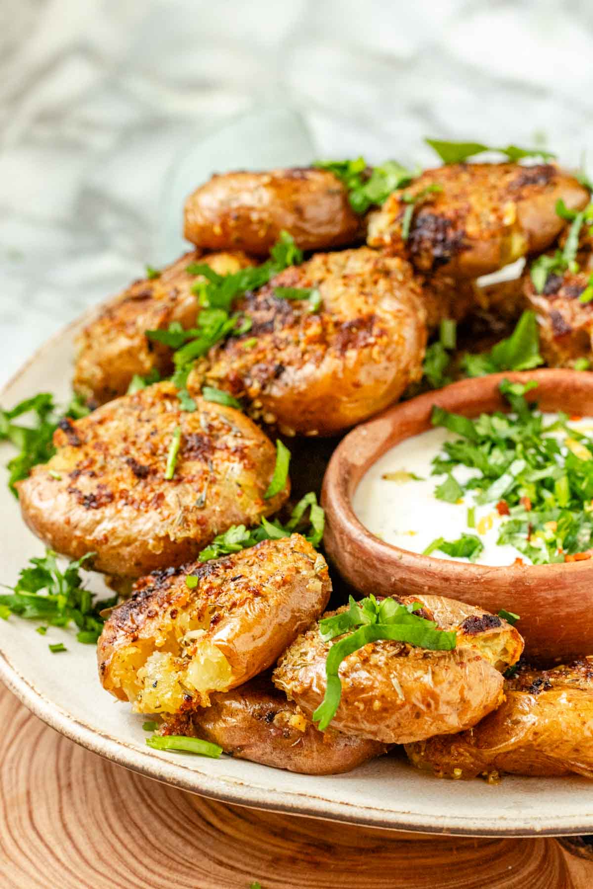 Smashed potatoes on a plate with a bowl of dip.