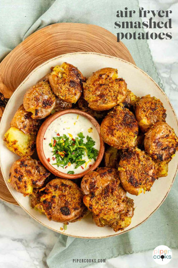 Smashed potatoes on a plate with a bowl of dip with text title for Pinterest.