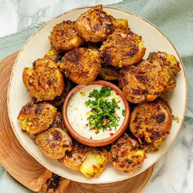 Smashed potatoes on a plate with a bowl of dip.