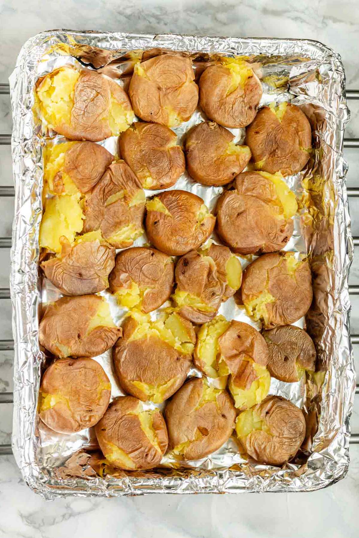 Smashed baby potatoes on a foil-lined baking sheet.