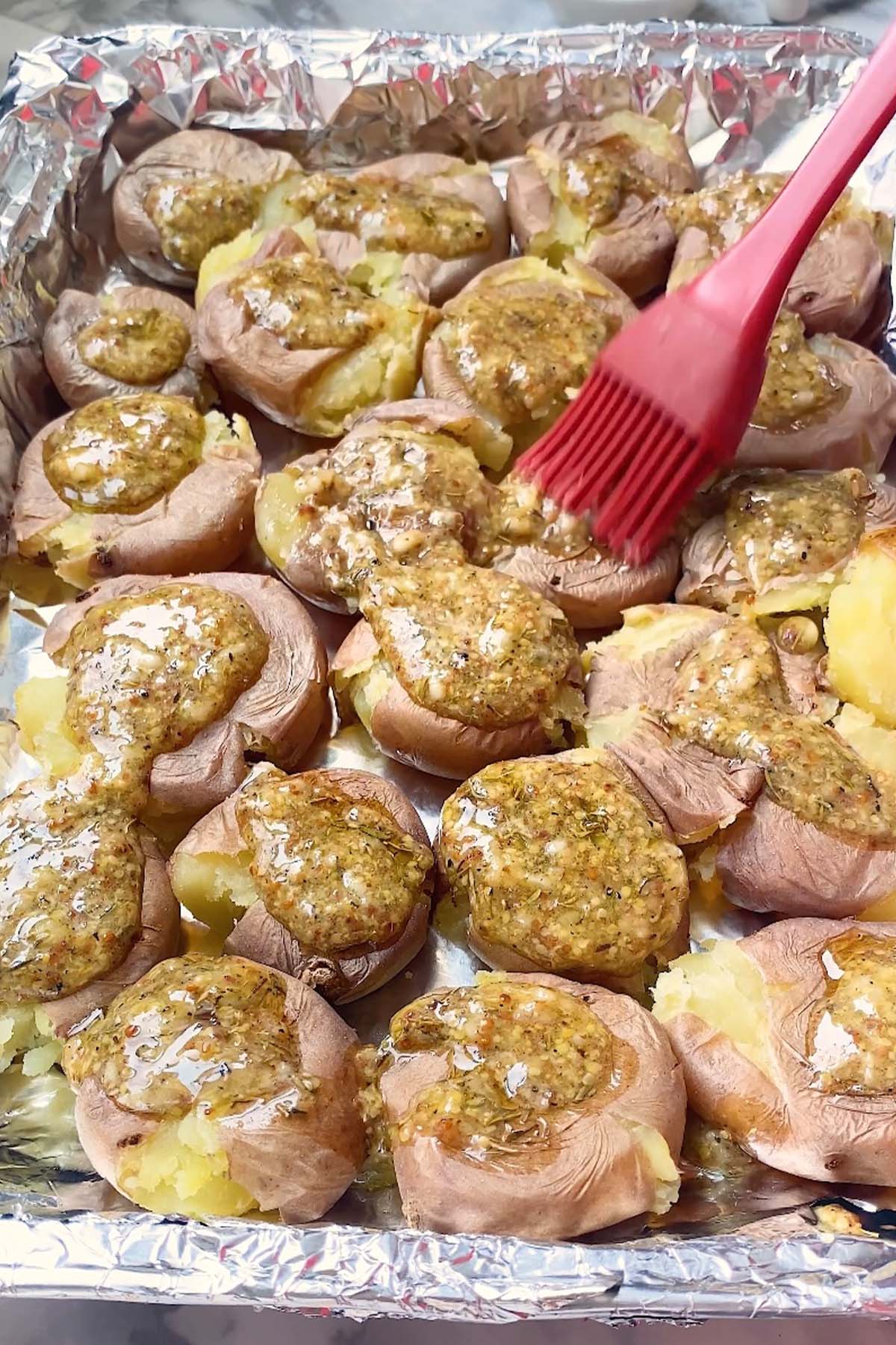 Mustard sauce is brushed on smashed baby potatoes on a foil-lined baking sheet.