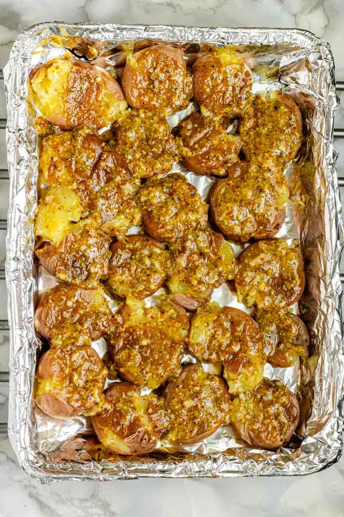 Smashed potatoes covered with mustard sauce on a foil-lined baking sheet.
