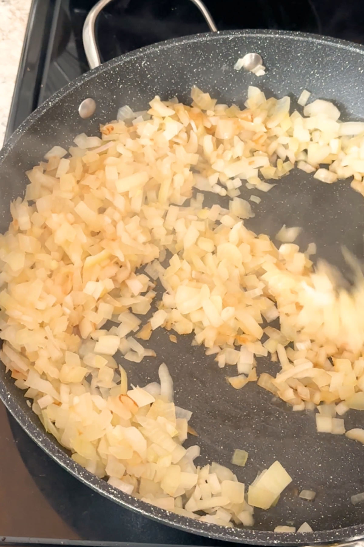 Onions are stirred in a skillet.