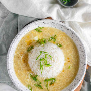 Egg drop soup in a bowl with a rounded ball of rice in the center and green onions on top.