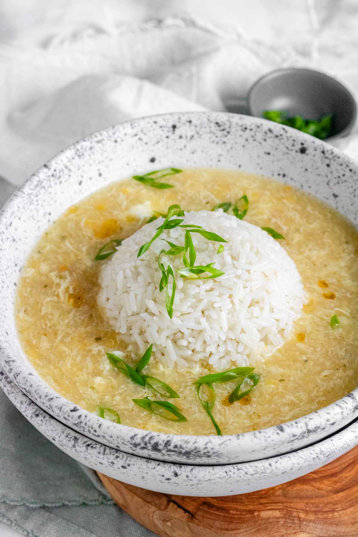 Egg drop soup in a bowl with a rounded ball of rice in the center and green onions on top.